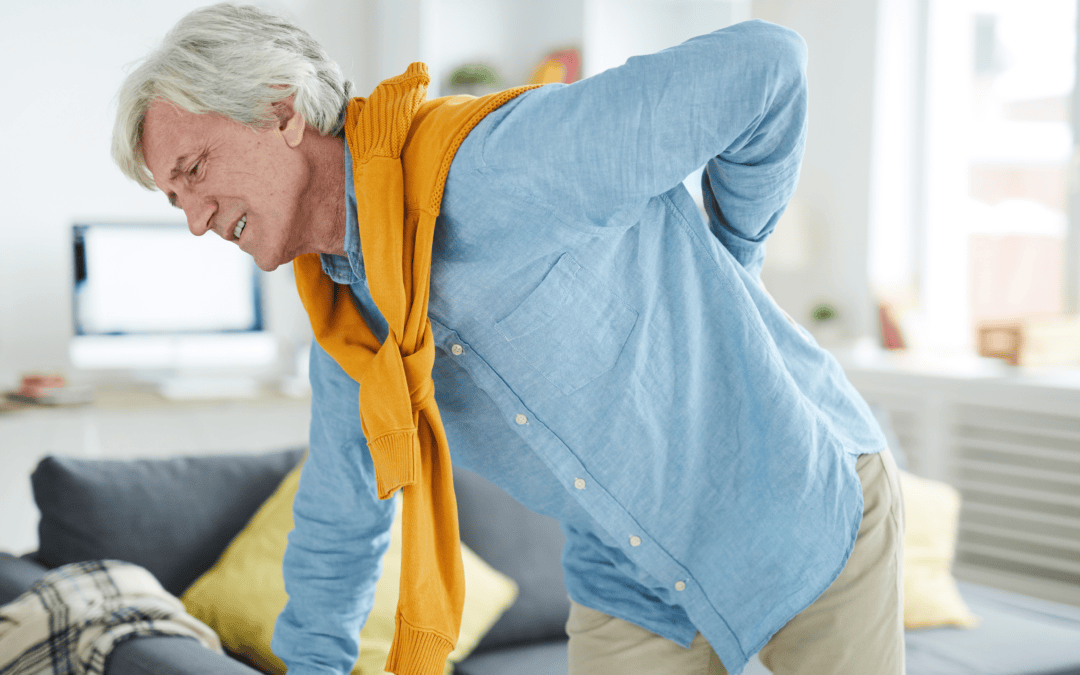 Elderly man experiencing lower back pain while shopping in a bright living room.